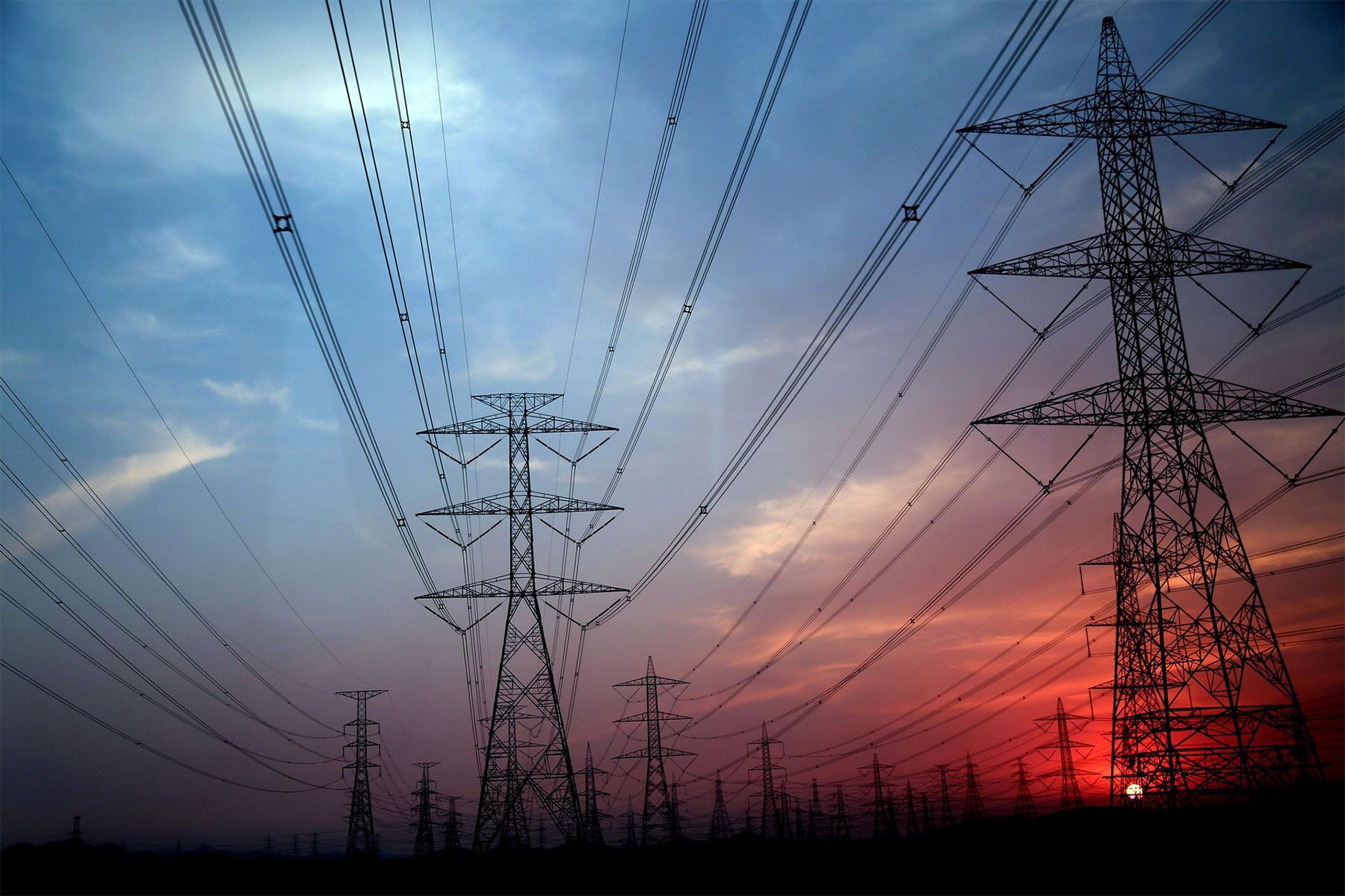 Lignes à haute tension au coucher du soleil, symbolisant l'infrastructure énergétique et son impact sur l'environnement. - Kunak