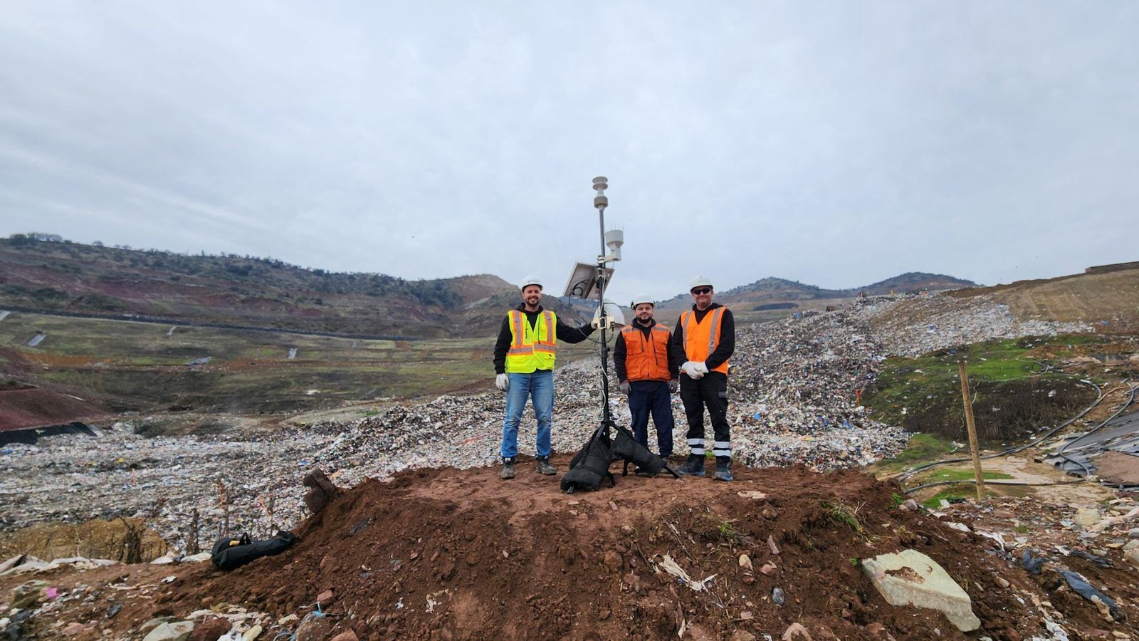 Technicians beside a Kunak station with weather sensors installed at a landfill to monitor odours. - Kunak